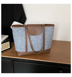 Detail view of denim fabric and brown leather stitching on a large tote bag