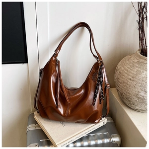 Brown oil wax leather tote bag with tassel pendant on silver suitcase and art books