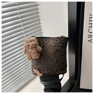Close-up of leopard print bucket bag featuring a plush bear charm and green leather straps