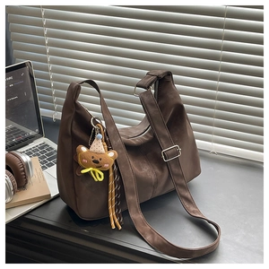 Close-up of wide strap with silver buckle and plush bear charm on a brown hobo bag