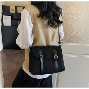 Detail of a black matte crossbody bag with gold buckles worn by a model in casual wear