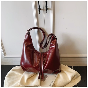 Detailed close-up of glossy wine red hobo bag with fringe zipper on white fabric