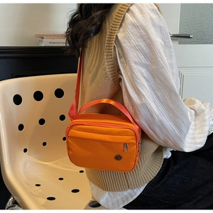 Detail showing the large orange nylon tote bag worn by a model in a minimalist setting