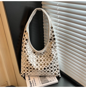 Détail du sac hobo blanc avec rivets argentés posé sur le rebord d'une fenêtre