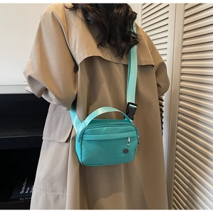 Detail of mint green nylon crossbody bag showing the adjustable strap and zipper pocket