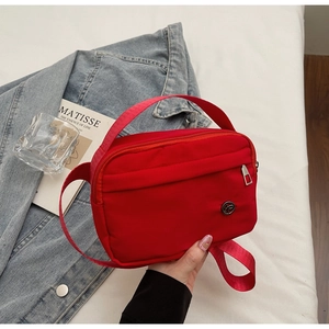 Close-up of lightweight red nylon square crossbody bag with zipper pocket and metal logo