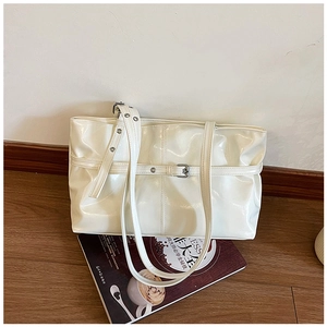 Close-up of white glossy patent leather tote bag with metallic eyelets and strap details