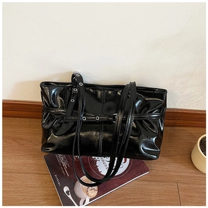 Detail of black glossy patent leather tote bag featuring stylish silver metal eyelet straps