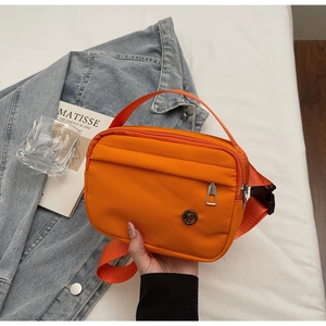 Detailed close-up of an orange nylon crossbody bag with silver zippers and adjustable strap