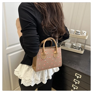 Détail du sac bandoulière à motif cerise porté par un mannequin en jupe de dentelle