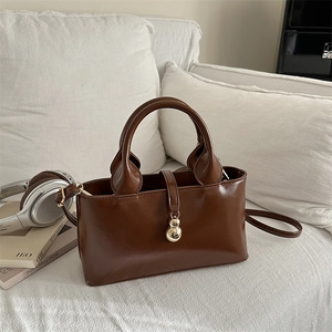 Borsa tote in pelle marrone lucida con ciondolo dorato su un divano bianco