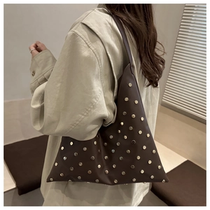 Detail view of brown faux leather shoulder bag with golden rivets worn by a model
