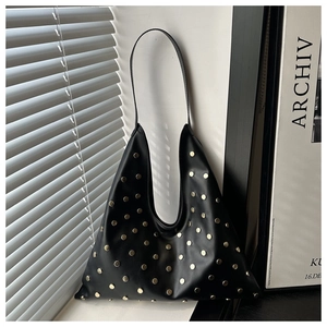 Detailed close-up of a black leather hobo bag with gold studs in natural window light