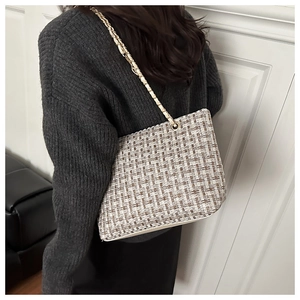 Detail of tweed checkered tote bag with gold chain strap worn by model on shoulder