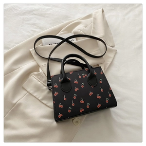 Détail du mini sac noir en cuir PU à motif cerise sur fond de blazer beige