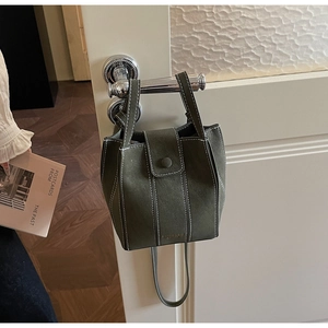 Detailed close-up of dark green bucket bag featuring white stitching and gold logo