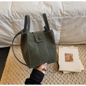 Close-up of a dark green leather bucket bag with contrast stitching and gold lettering