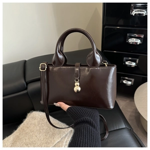 Détail d'un sac à main marron foncé avec finition brillante et breloque dorée