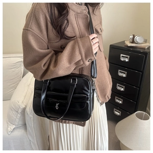 Detail of glossy black Boston bag with bow and heart metal pendant in casual setting