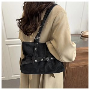 Detail of black suede shoulder bag with silver grommets and belt buckle straps