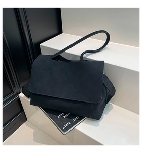 Close-up of minimalist black matte tote bag with wide woven strap on white steps