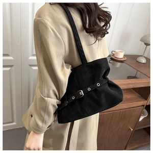 Side view of a black leather shoulder bag with silver buckle details on a trench coat