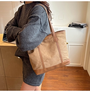 Detail of a large beige suede and brown leather tote bag worn by a model in a warm setting