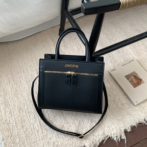Chic black crossbody tote bag with gold hardware and textured finish on white rug