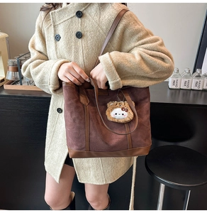 Detail of a brown suede tote bag featuring contrast leather trim and a cute plush cat charm