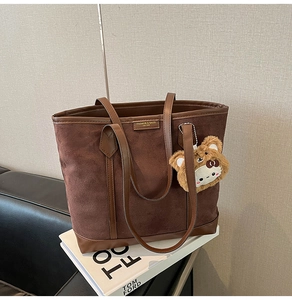 Detail of dark brown suede tote bag with leather handles and cute plush bear charm