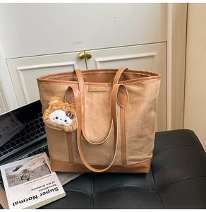 Detail of large brown tote bag with plush cat charm on a leather seat background