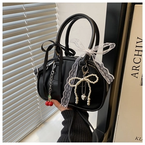 Close-up of black leather handbag featuring red cherry charm and pearl bow details