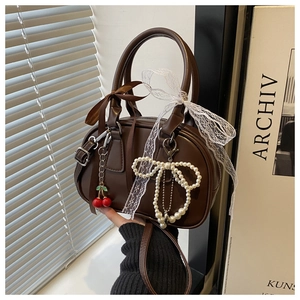Detailed side view of brown leather bow handbag with cherry and pearl pendants