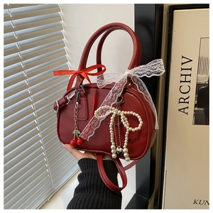 Detail of red Boston bag featuring lace trim, satin bows, and pearl cherry charms