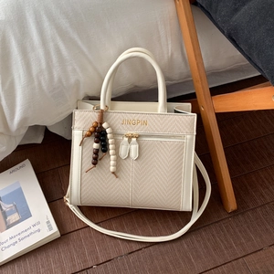 Chic cream woven tote bag featuring beaded tassels and gold lettering on a wooden floor