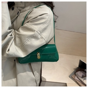 Détail du sac bandoulière vert foncé brillant avec un fermoir doré cylindrique en métal