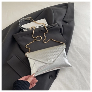 Detail of silver envelope clutch with pleated texture and golden chain on a grey suit