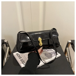 Détail d'un sac baguette en cuir verni noir avec un fermoir doré ovale en métal poli