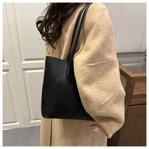 Detail of minimalist black matte leather tote bag worn with a classic wool coat
