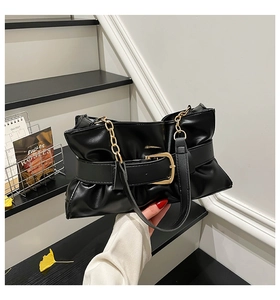 Détails d'un sac cabas noir plissé avec boucle dorée et bandoulière chaîne sur un escalier