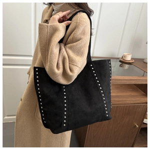 Detail of black suede tote bag with silver metal studs worn with a camel wool coat