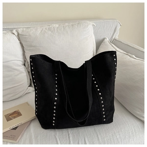 Detail of silver rivets on black faux suede tote bag on a minimalist white sofa