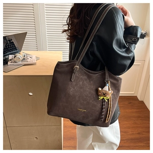 Detail of dark brown leather tote bag with white stitching and bear charm accessory