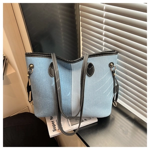 Detail of a denim tote bag showing leather patchwork and metallic side buckle accents