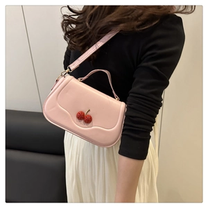 Detail of pink crossbody bag with red cherry ornaments worn with white pleated skirt