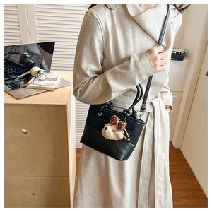 Detail of black leather crossbody bucket bag with cute plush animal charm in a cozy setting