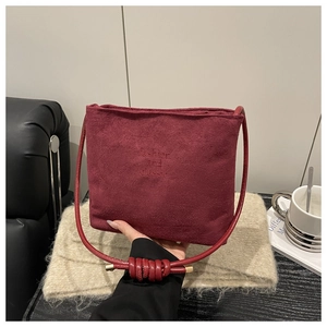 Close-up of wine red suede handbag featuring embossed lettering and knotted strap details