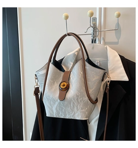 Close-up of pleated silver tote bag with vintage amber buckle and brown handle