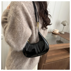 Side view of a glossy black patent leather crescent bag worn by a model in a cozy setting