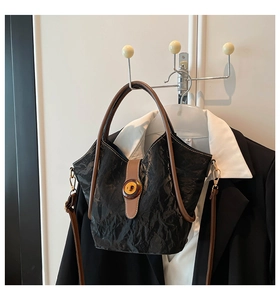 Detail of black pleated bucket bag with amber twist lock and contrast brown handle straps
